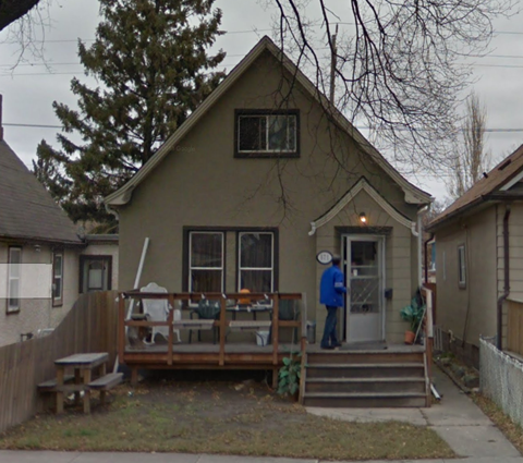 A man in a blue jacket is standing on the porch of a house.