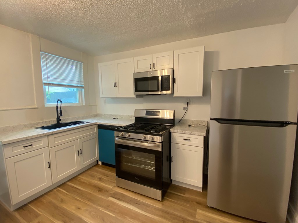 A kitchen with a stove, oven, refrigerator, and cabinets.