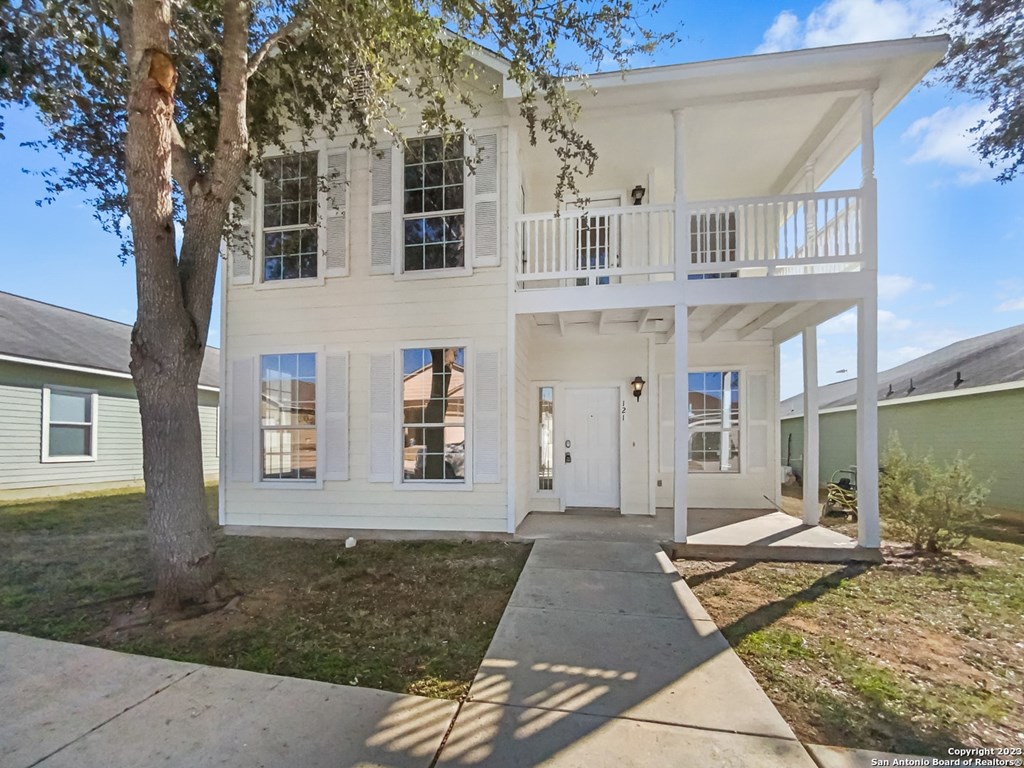 A white two-story house with a balcony and a tree in front.