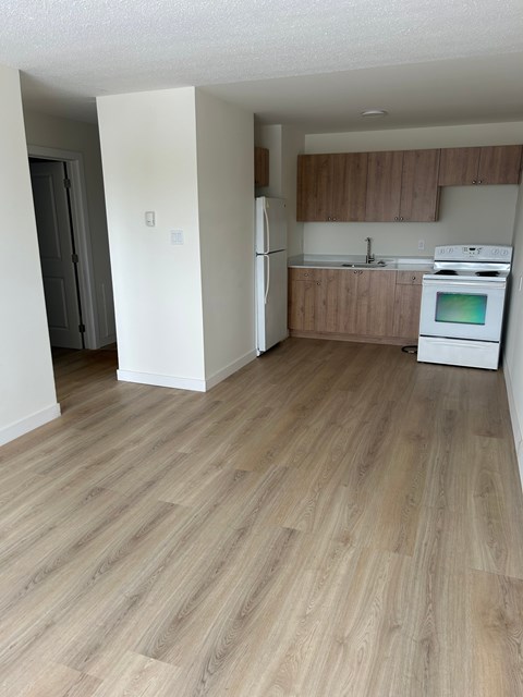 A kitchen with a white fridge and oven, and wooden flooring.