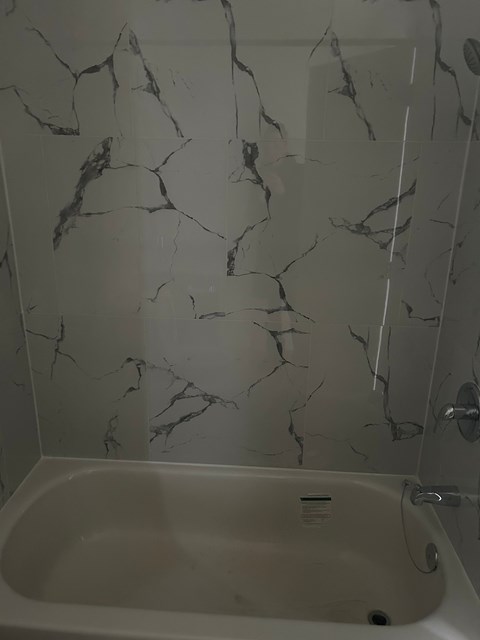 A white bathtub with a marble wall behind it.