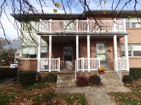 A house with a white porch and a tree with leaves hanging over it.