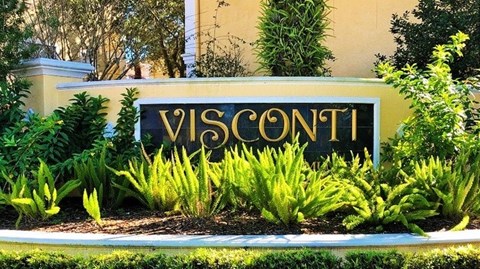 A sign that says "VISCONTI" in front of a building surrounded by plants.