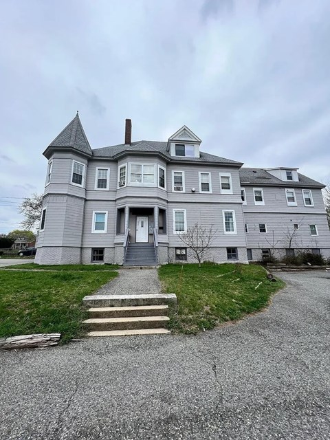 A large grey house with a tower and a front porch.