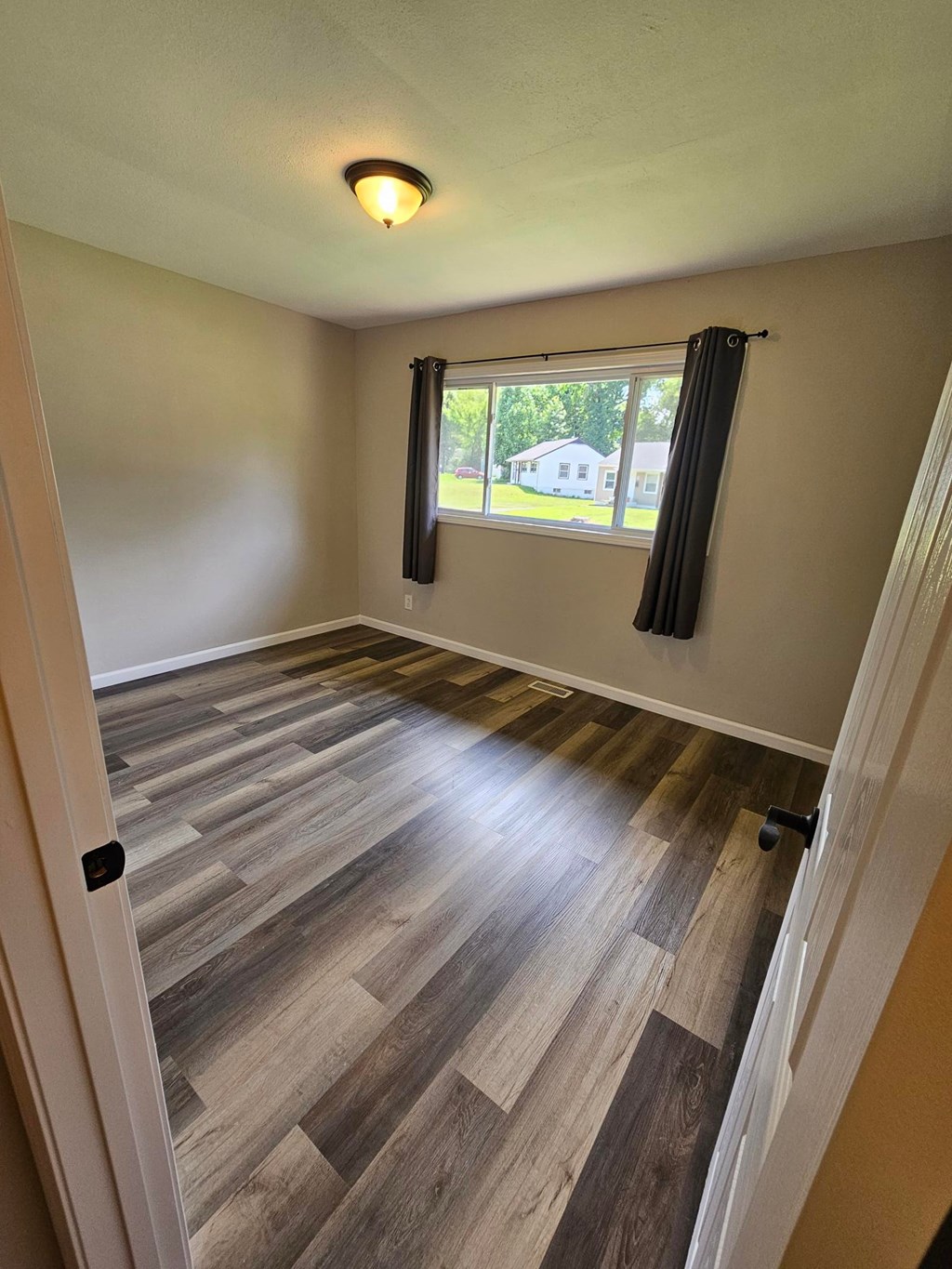 A room with wooden flooring and a window with black curtains.