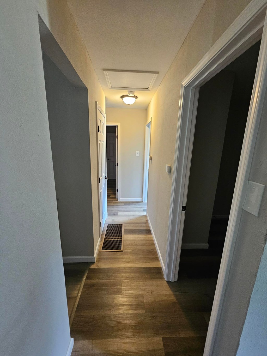 A long hallway with a light on the ceiling and a door at the end.