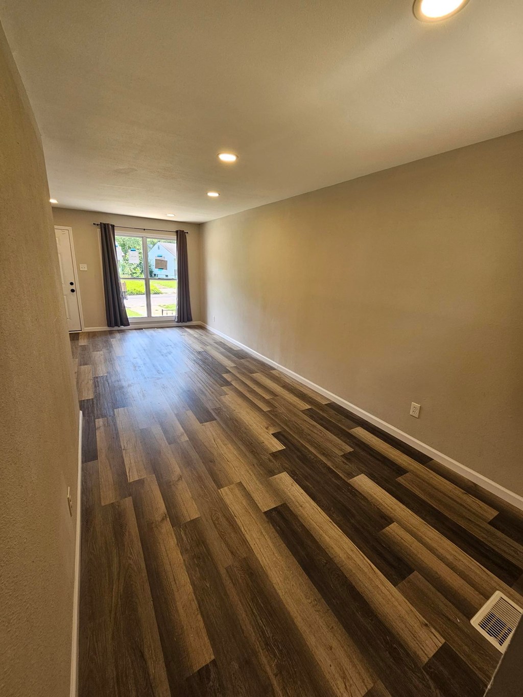 A long hallway with wooden floors and a window at the end.