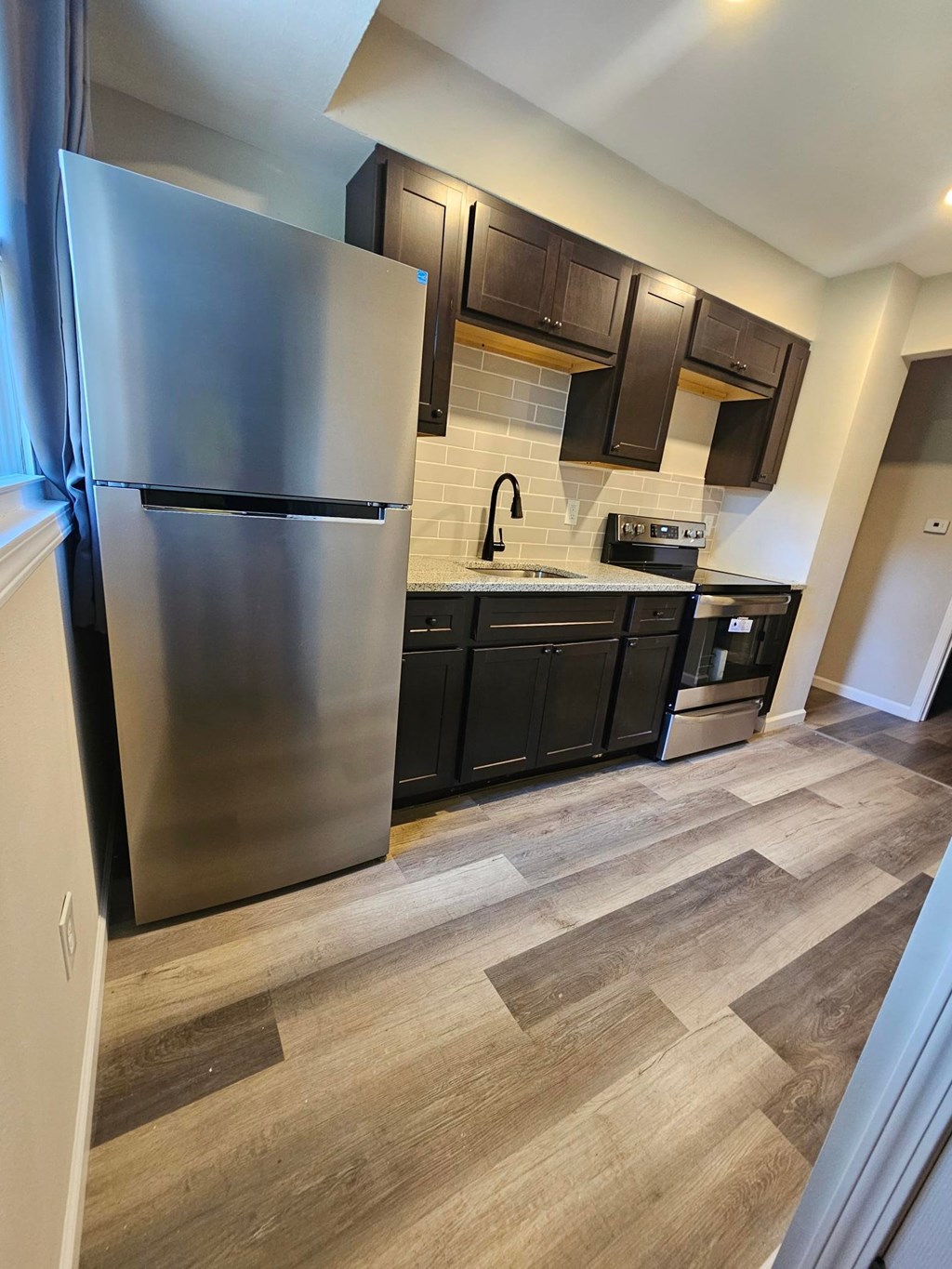 A kitchen with a stainless steel refrigerator and wooden flooring.