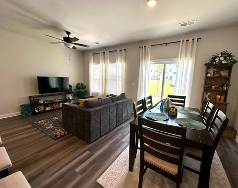 A living room with a grey couch, a black television, and a dining table with chairs.