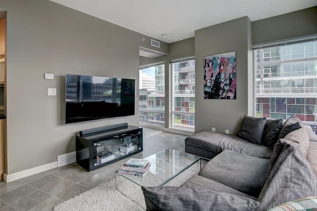 A living room with a grey couch and a flat screen TV mounted on the wall.