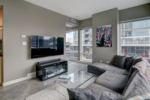 A living room with a grey couch and a flat screen TV mounted on the wall.