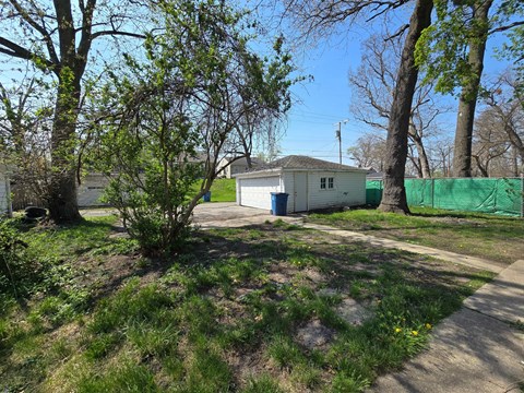 A small white house with a blue door is surrounded by trees and grass.