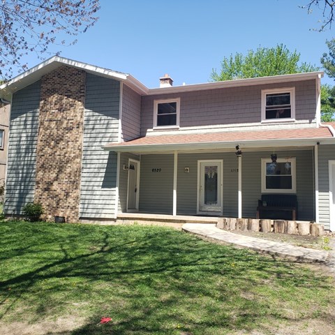 A house with a grey and pink facade has a number 6520 on the front door.