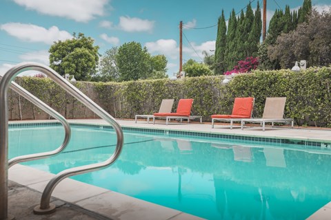 A pool with a metal ladder and two red chairs.