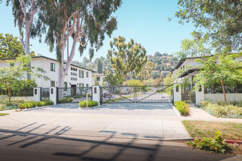 A gated entrance to a residential area with trees and houses in the background.