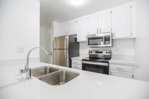 A kitchen with a stainless steel sink and white cabinets.