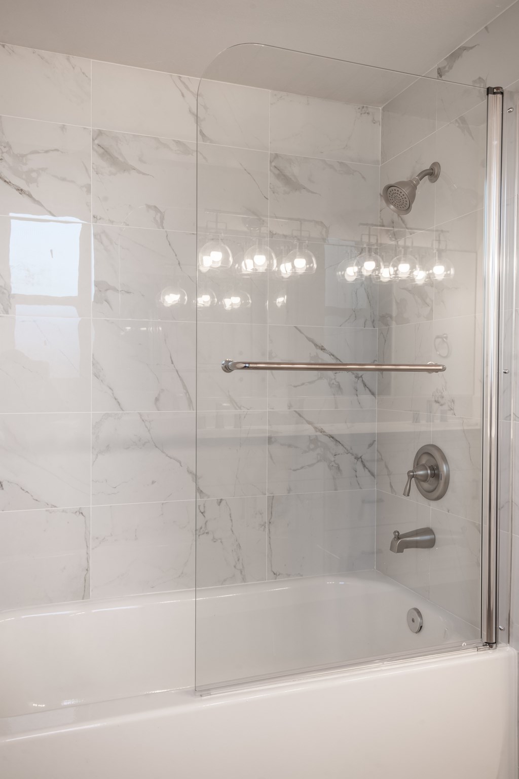 A white marble tiled shower with a glass door and a shower head.