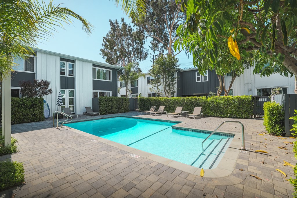 A swimming pool surrounded by a brick patio and lounge chairs.
