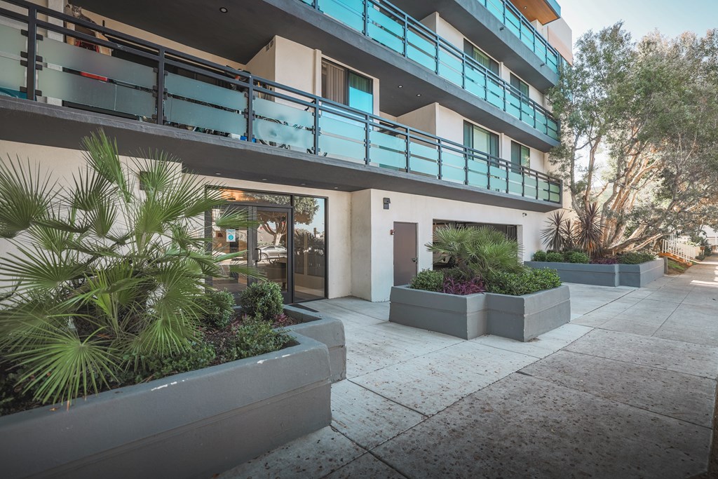 A modern building with a balcony and plants in front.