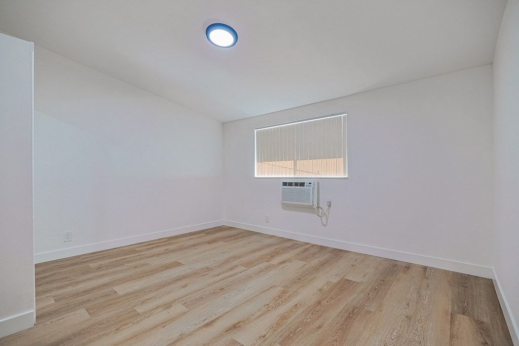 A room with a wooden floor and a window with blinds.