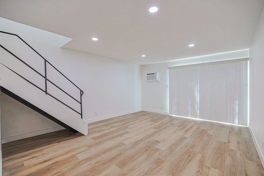 A room with wooden flooring and a staircase with a black railing.