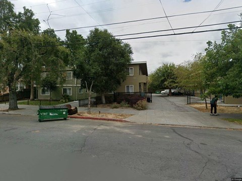 A street view with a green trash bin on the sidewalk.