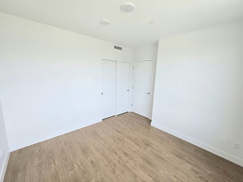 A room with white walls and wood flooring with two doors.