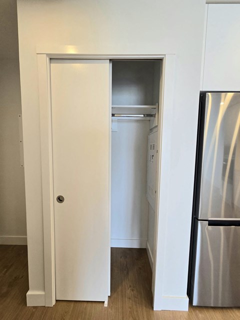 A white door is open to reveal a small kitchen with a refrigerator.