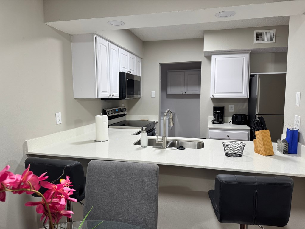 A kitchen with a white countertop and black chairs.