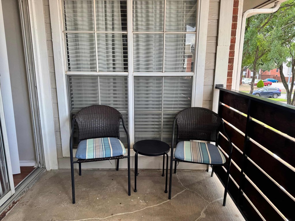 Two chairs and a table are on a porch.
