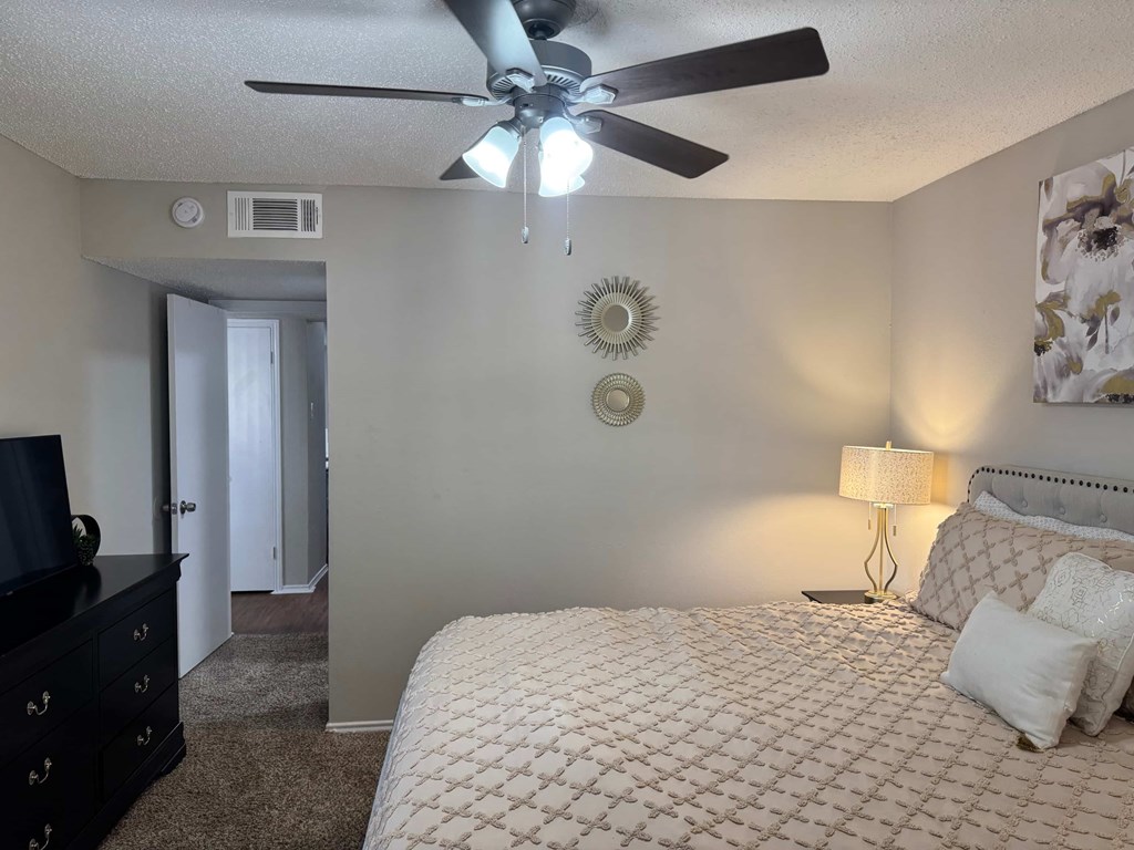 A bedroom with a bed, dresser, and ceiling fan.