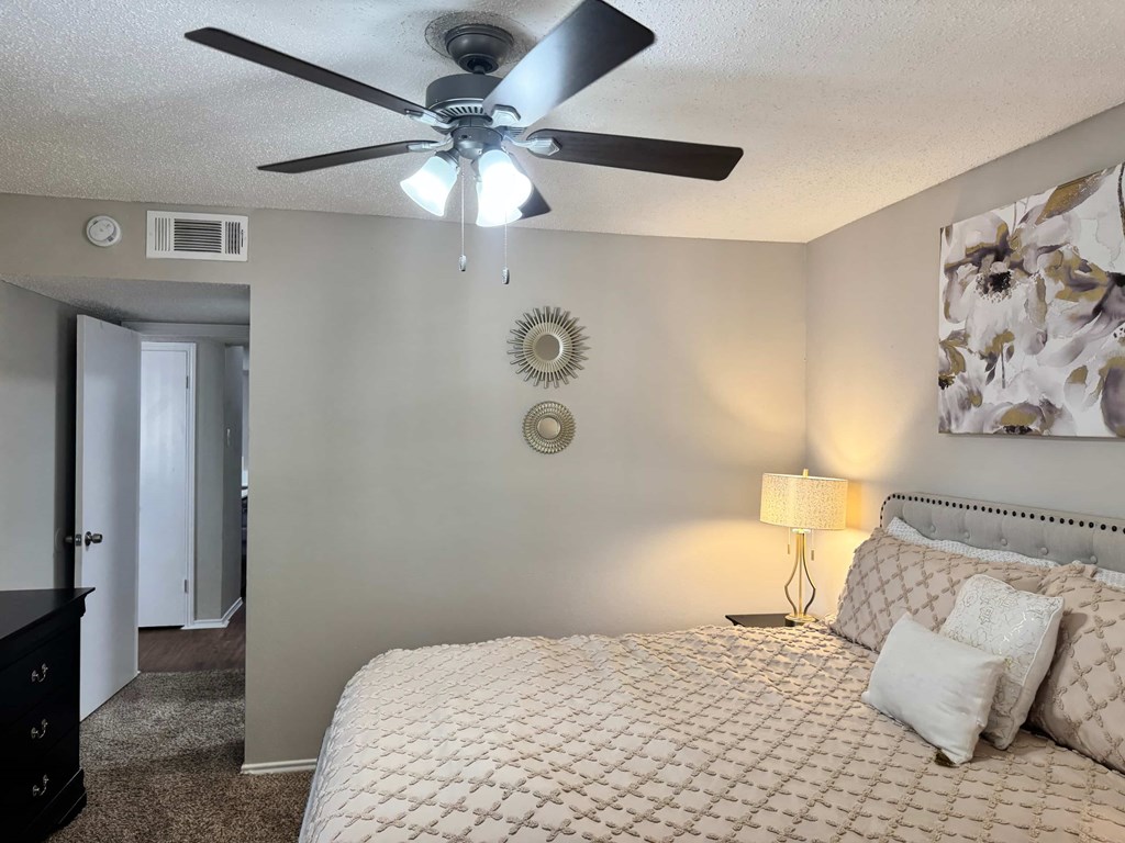 A bedroom with a bed, lamp, and a ceiling fan.