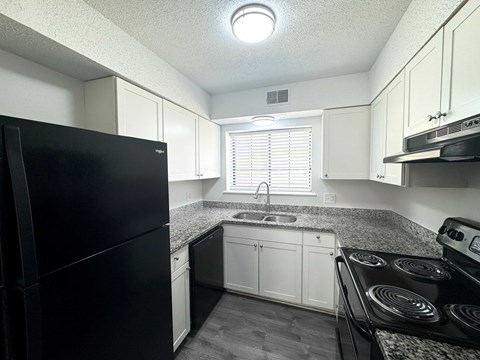 A black refrigerator is in a kitchen with white cabinets.