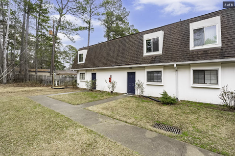 A white house with a black door and windows is surrounded by a grassy area and trees.