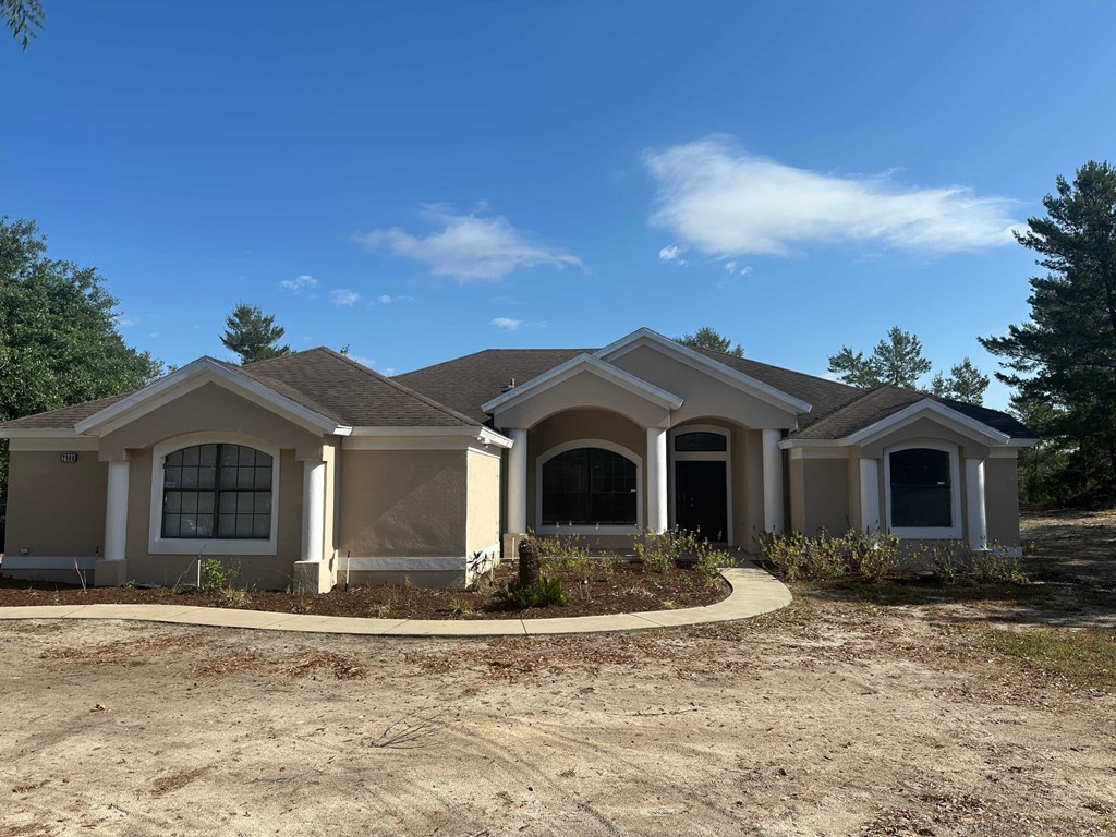 A house with a brown roof and white walls is surrounded by a dirt area.