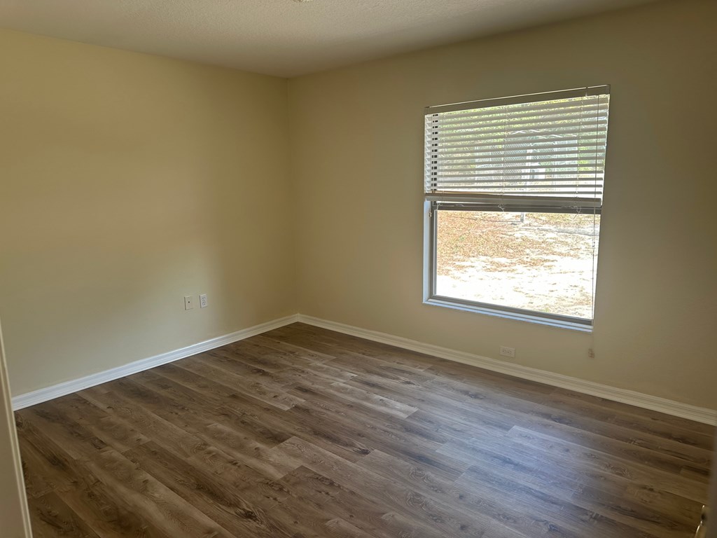A room with wooden flooring and a window with blinds.