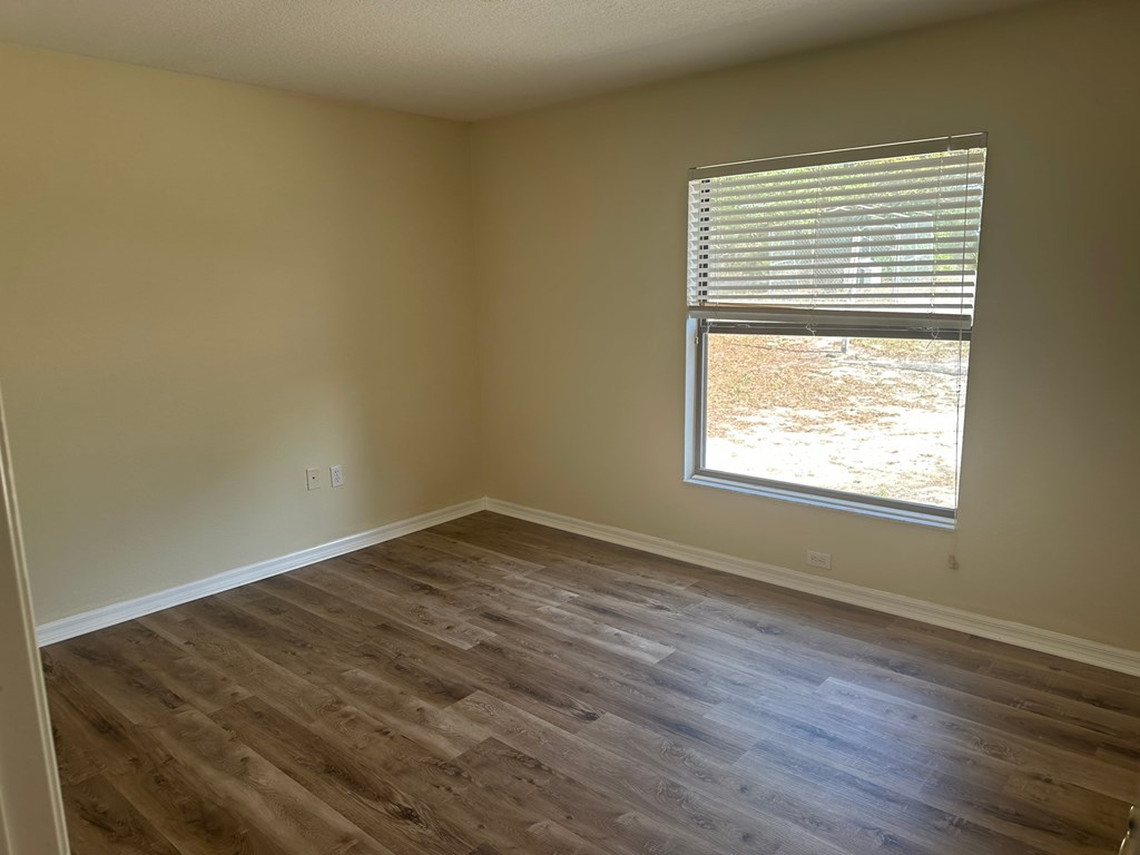 A room with wooden flooring and a window with blinds.