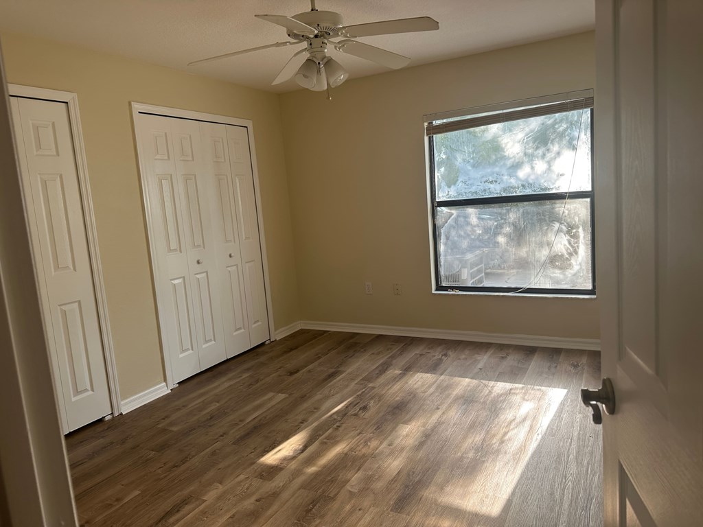 A room with a ceiling fan and a window with a view of trees outside.