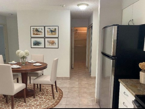 A kitchen with a table set for two and a fridge to the right.