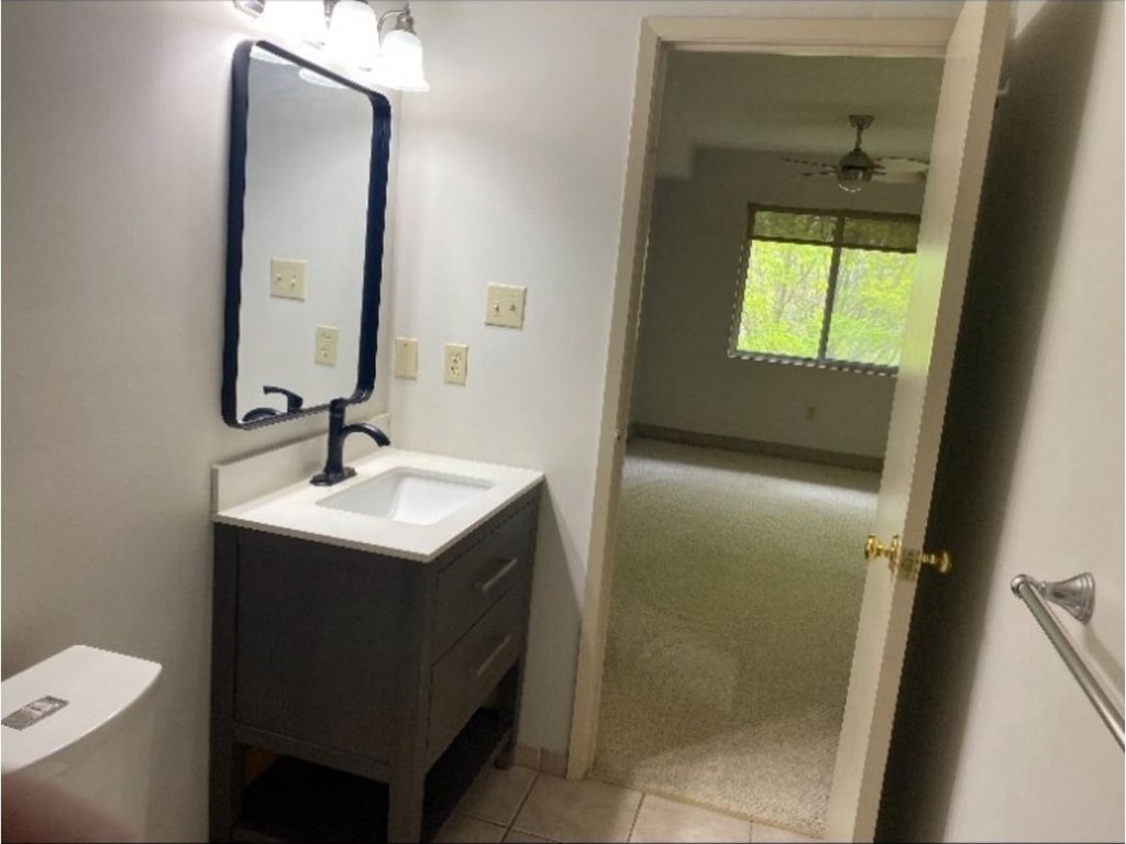 A bathroom with a sink, mirror, toilet and a door leading to a hallway.