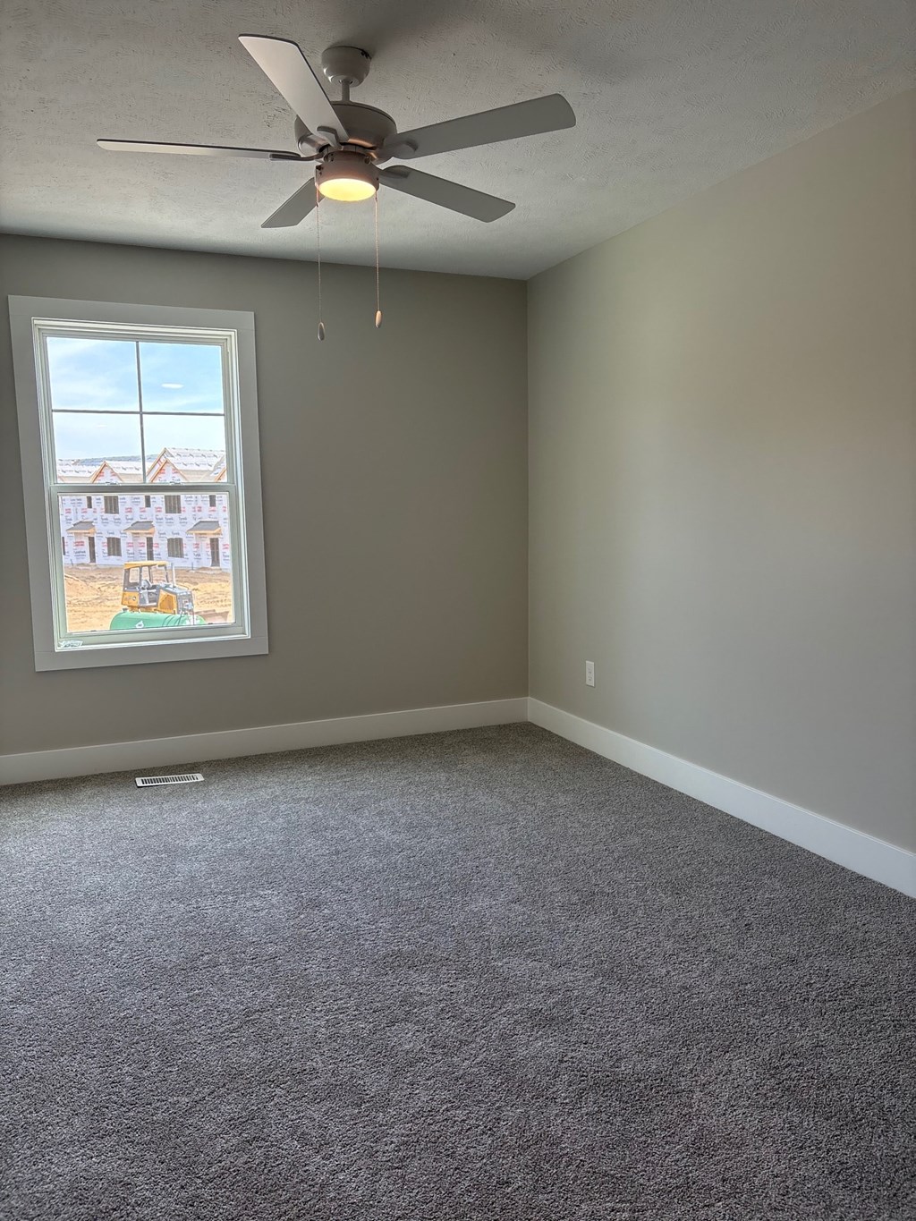 A room with a ceiling fan and a window overlooking a construction site.