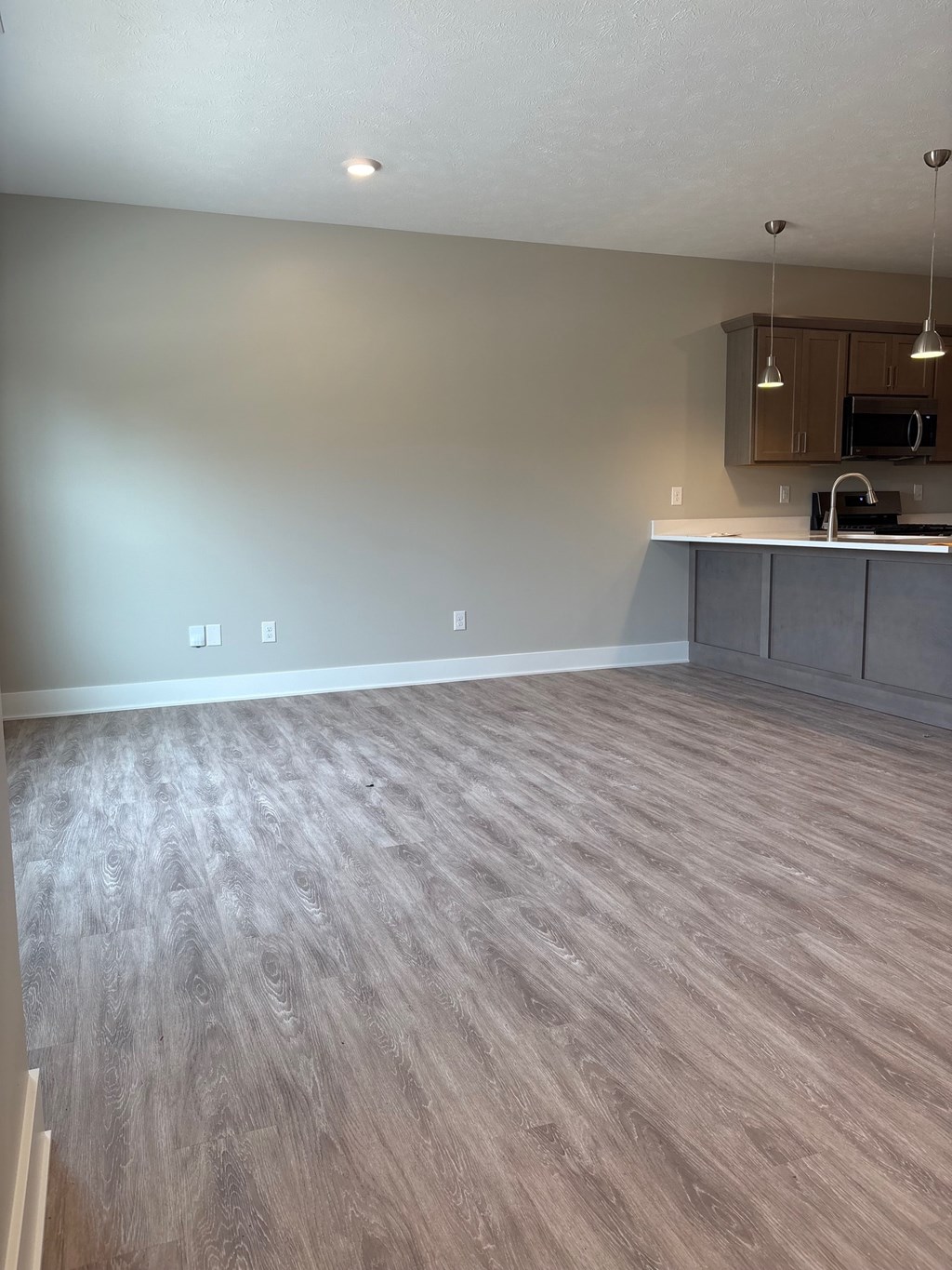 A room with a wooden floor and a kitchenette in the background.