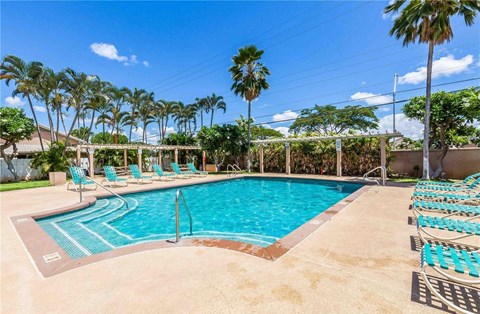 A pool surrounded by palm trees and lounge chairs.