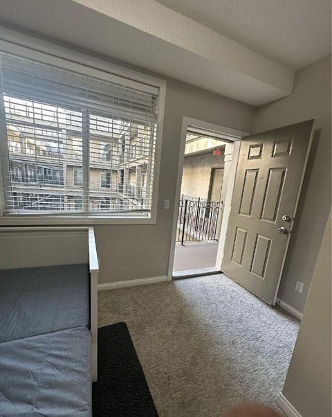A bedroom with a bed, carpet, and a door leading to a balcony.