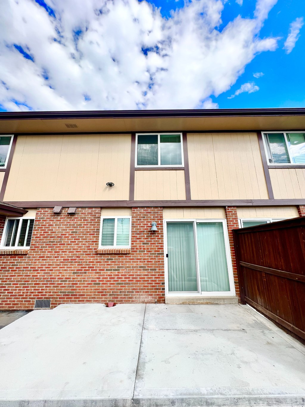 A house with a brown brick wall and a tan siding wall with a glass door and window.