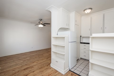 A white kitchen with a refrigerator, cabinets, and a ceiling fan.