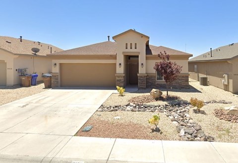 A house with a brown roof and tan walls has a driveway in front.