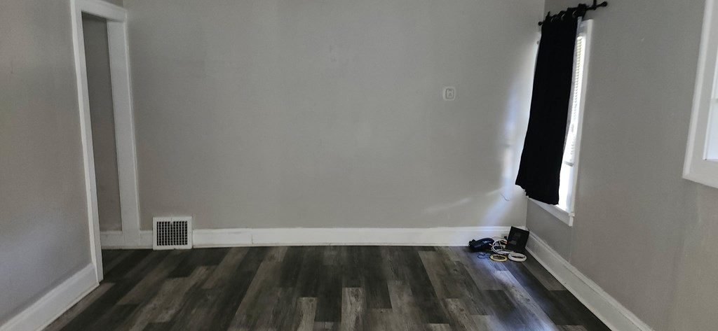 A room with a wood floor and a window with black curtains.