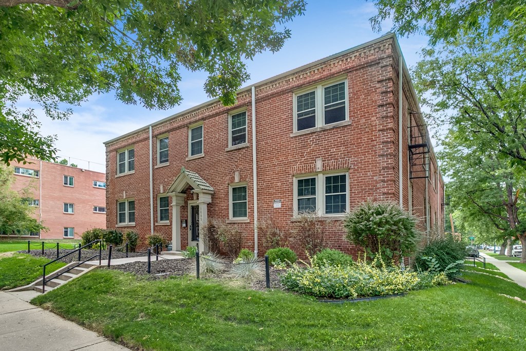 A red brick building with a black fence and green bushes in front.