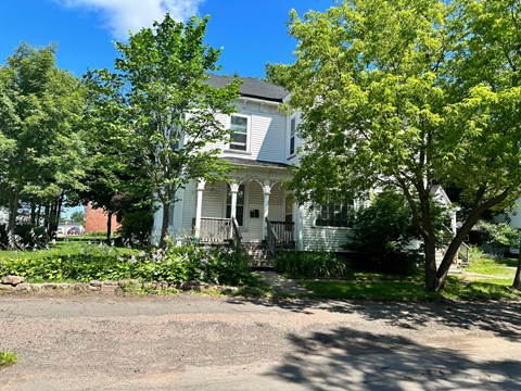 A white house with a porch and a tree in front.